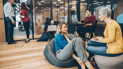 Plusieurs personnes en groupe, dans un salle faisant su coworking sur des poufs