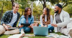 Un groupe d'étudiants assis dans l'herbe avec du matériel d'apprentissage devant eux, tablettes, ordinateurs, feuilles et livres. Le groupe d'étudiants est constitué de deux filles et deux garçons, dans une ambiance légère et joyeuse - Cowoliday