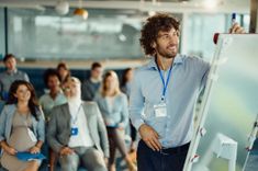 Un homme en premier plan faisant une présentation interactive en écrivant sur un paperboard lors d'un séminaire, ses collaborateurs dans le fond sont engagés et à l'écoute et installé dans une espace moderne - Cowoliday