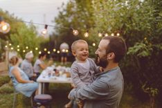 Un père qui tient son fils dans les bras lors de son baptême ou sa communion, on voit en arrière plan le reste de la famille et des amis célébrez l'occasion sacré - Cowoliday